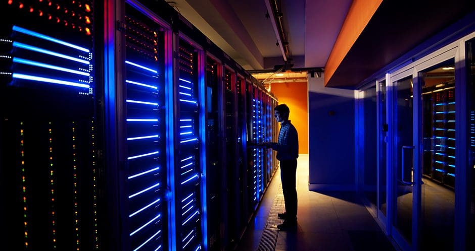 A man standing in a server room with blue lights.