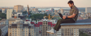 A man sitting on top of a building with a laptop.