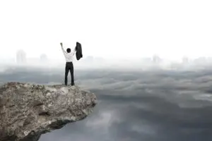 A businessman standing on top of a cliff with his arms raised.