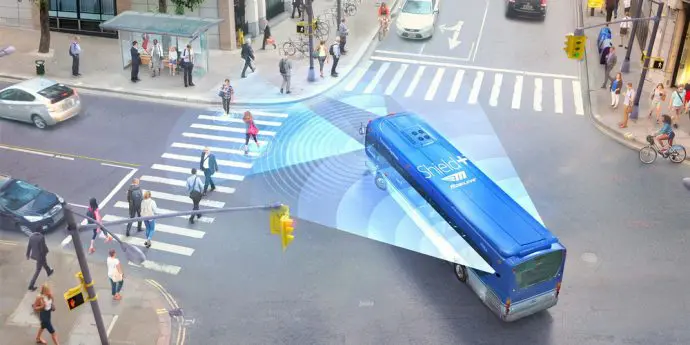 A blue bus driving down the street with people crossing it.